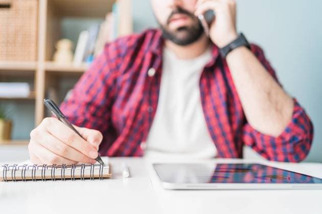 An anonymous man is writing in a notebook. The man is working from home. The entrepreneur is talking on the mobile phone, Model released, Property released Copyright: xAlvaroxSanchezx MR
