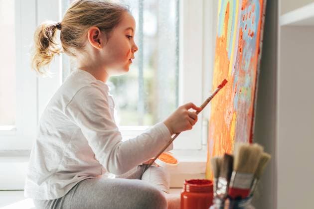 IMAGO Kreativ: Bildung, Kunsterziehung Creative blond girl in casual clothes sitting on window sill against window and painting with paintbrush large multi colored rainbow on orange canvas, Model released, Property released Copyright: xAngelxSantamariax MR