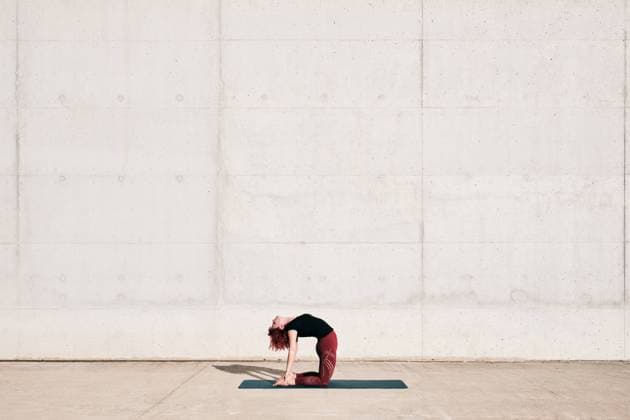 IMAGO Creative, Urban Lifestyle Trendy fit woman in sportswear doing yoga in camel pose on sports mat alone on street against concrete wall in sunny day Copyright: xAntonioxOvejerox Model Released