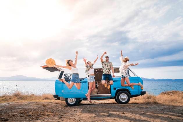 Cheerful tourist jumping raising hands and legs on background of bright minivan on beach in sunny day Copyright: xJuanxMiguelxApariciox Model Released