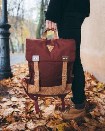 Side view of crop modern female in casual black wear holding stylish backpack while standing on sidewalk covered with fallen leaves in autumn day in city, Model released Copyright: xCarlosxForteax MR