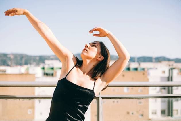 Graceful female dancer in moment of performing element with outstretches arms looking up on summer terrace on background of palm trees Copyright: xDanixNavarrox Model Released