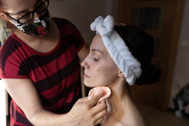 IMAGO Creative: Neue Aussichten Crop anonymous makeup artist in protective mask and casual wear applying foundation with cotton pad on face of young actress with white headband, Model released Copyright: xDanixSerranox MR