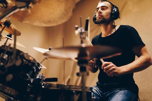 Positive handsome male with headphones playing on drums in studio Copyright: xDavidxGailx Model Released