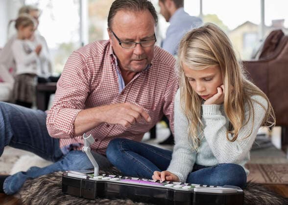IMAGO Creative: Bildung, Musikerziehung Grandfather and granddaughter playing piano with family in background at home , model released Copyright: xMaskotx , MA38866