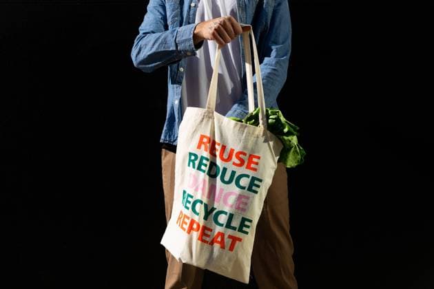 Crop anonymous male buyer holding fabric shopping bag with text message of reuse and recycle concept on black background, Model released, Property released Copyright: xDavidxMunozx MR