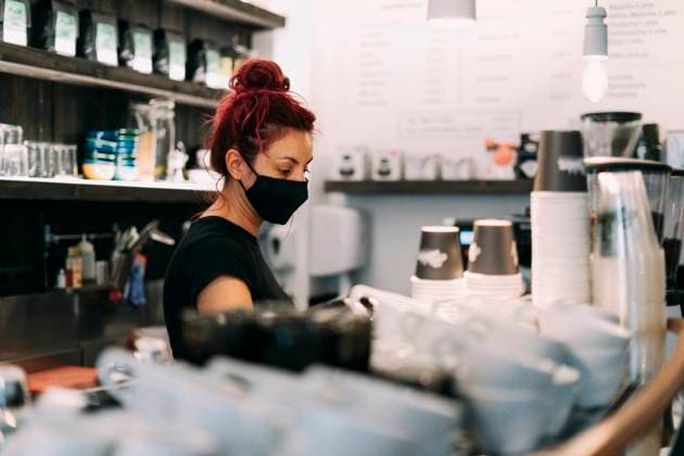 IMAGO Creative: 2021 Trends Side view of female bartender in face mask standing at counter in coffee shop and making delicious hot beverage in coffee machine during coronavirus epidemic Copyright: xDavidxMunozx Model Released