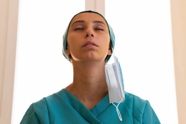 Low angle of tranquil female medic in uniform standing in clinic without mask and breathing in fresh air with closed eyes after coronavirus outbreak Copyright: xDavidxMunozx Model Released