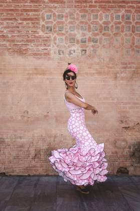Side view of eccentric cheerful woman in colorful pink costume smiling and dancing by brick wall on sunny day Copyright: xEduardoxLopezx Model Released