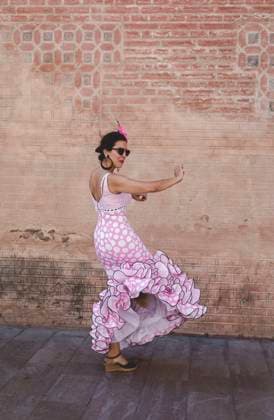 Side view of eccentric cheerful woman in colorful pink costume smiling and dancing by brick wall on sunny day Copyright: xEduardoxLopezx Model Released