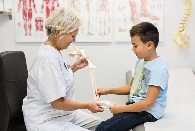 Senior female orthopedist showing hand model to boy at clinic , model released Copyright: xMaskotx , MA43079