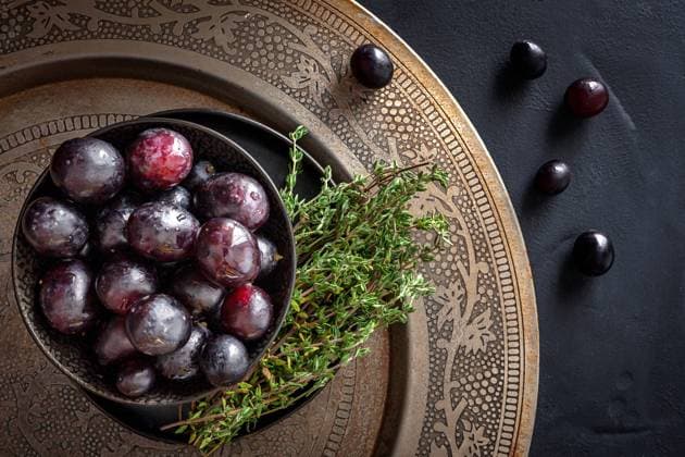 From above bowl filled with delicious ripe red grapes placed with fresh green thyme sprigs on ornamental platter on black table Copyright: xEduardoxLopezx Model Released