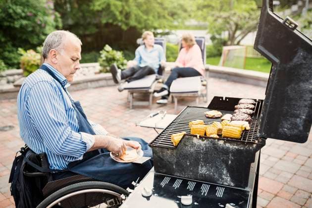 Disabled man barbecuing while family sitting in background at yard , model released, property released Copyright: xMaskotx , MA45444