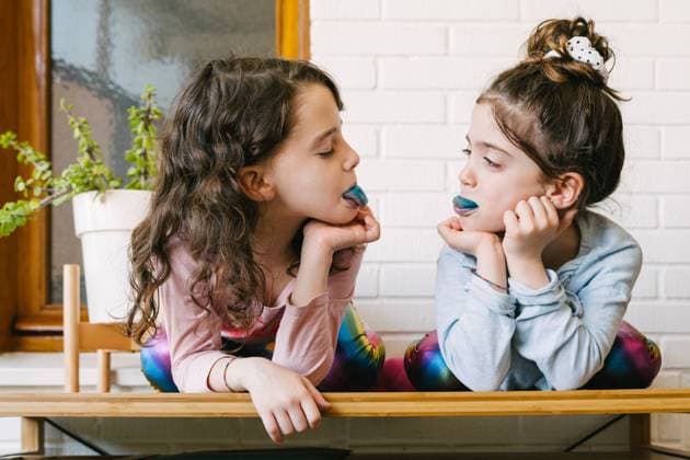 Two smiling sisters sticking out a blue tongue after eating a blue bubble gum Copyright: xEloisaxRamosx Model Released
