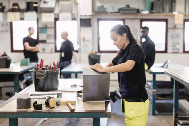 Side view of female student working on sheet metal with coworkers in background , model released, property released Copyright: xMaskotx , MA48316
