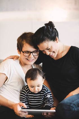 Smiling lesbian couple and baby girl looking in digital tablet at home , model released Copyright: xMaskotx , MA49059