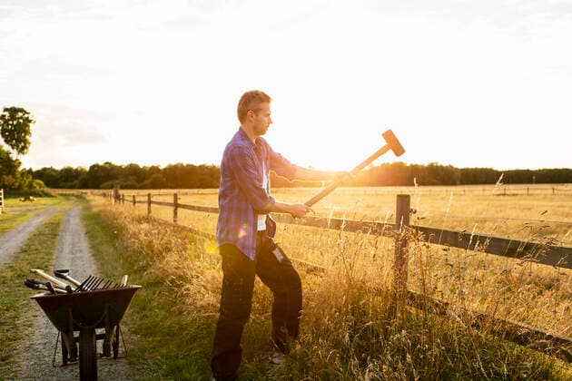 IMAGO Creative: Landleben, Mit Nachhaltigkeit grün auf dem Land leben Man hammering fence on grassy field during sunny day , model released, property released Copyright: xKentarooxTrymanx , MA49095