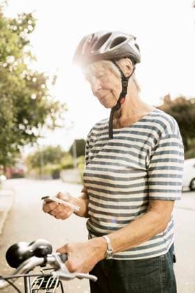 Senior woman using phone while standing with bicycle on road , model released Copyright: xKentarooxTrymanx , MA49748