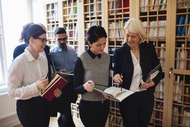 Smiling lawyers discussing while walking by bookshelf in library , model released Copyright: xMaskotx , MA49994