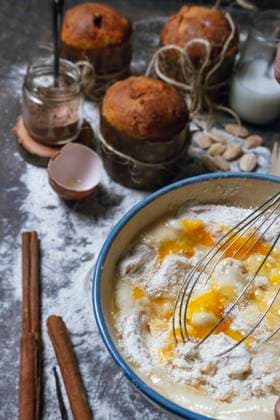 Housewife with whisk mixing products in ceramic bowl while preparing dough for typical Christmas panettone cake on table with baked panettone and ingredients Copyright: xFatimaxGuisadox Model Released