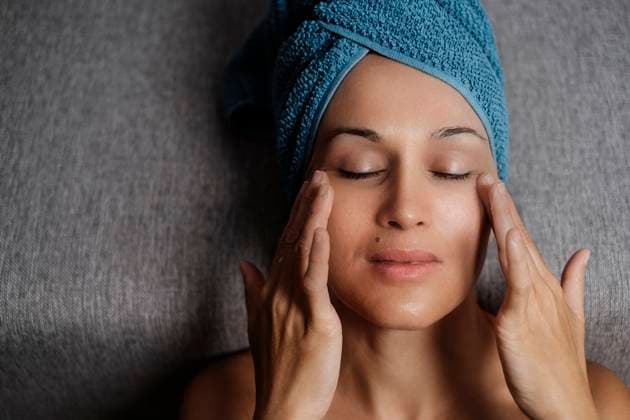IMAGO Creative: Clickbait, Hautpflege und Kosmetik Charming young female with bare shoulders and towel on head smearing facial skincare cream on face during makeup procedure at home with eyes closed Copyright: xFaustinoxCarmonax Model Released