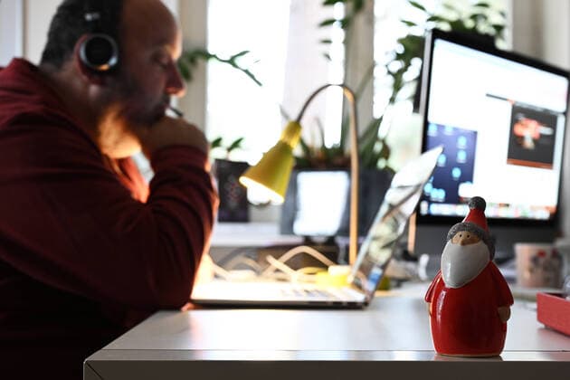 Homeoffice- Mann sitzt zu Hause an seinem Laptop und arbeitet. An seinem Arbeitsplatz steht ein Weihnachtsmann.