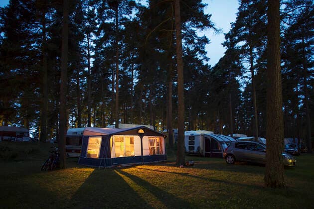 IMAGO Creative: Klimawandel - Nachhaltiges Reisen Caravans parked in travel trailer park by illuminated tent amidst trees at dusk Copyright: xKentarooxTrymanx , MA52568