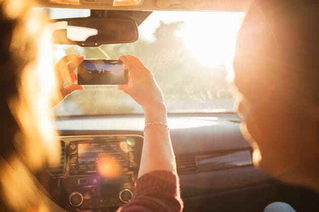 IMAGO Creative: Klimawandel - Nachhaltiges Reisen Man looking at woman photographing from mobile phone through car windshield , model released Copyright: xMaskotx , MA53205