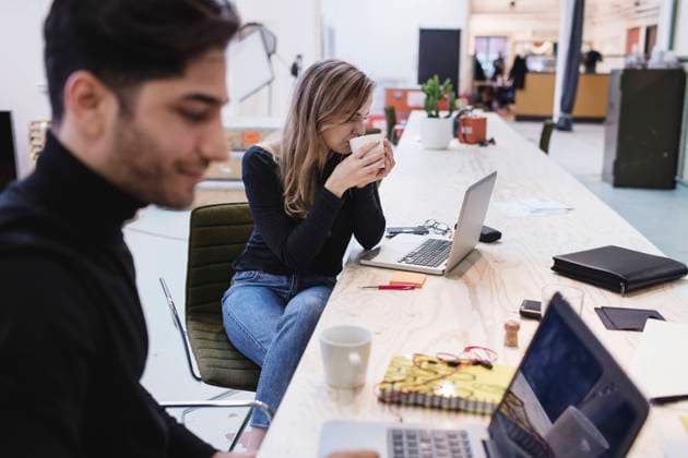 Young woman drinking coffee while sitting with colleague at desk in office , model released, property released Copyright: xMaskotx , MA54515