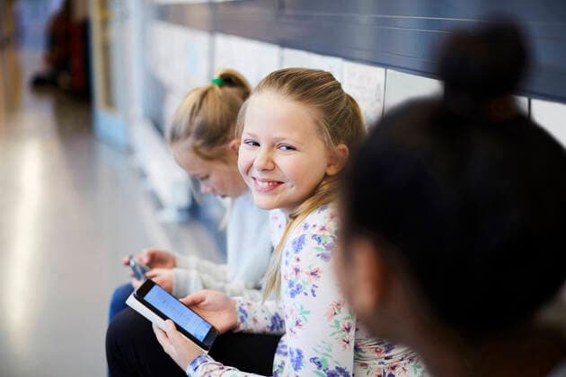 Smiling girl holding smart phone while looking at friend in school corridor , model released, property released Copyright: xMaskotx , MA55052