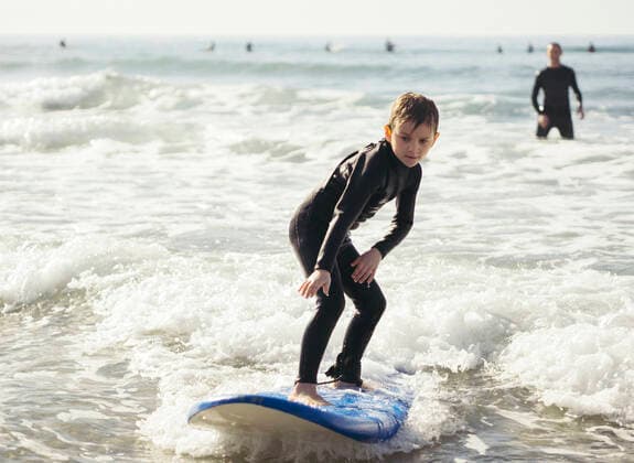 Full length of boy surfing in sea with father in background , model released Copyright: xMaskotx , MA56144