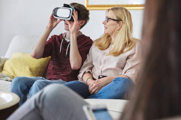 Mother looking at son using virtual reality headset while sitting on sofa , model released, property released Copyright: xMaskotx , MA56185