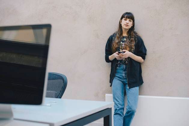Portrait of female computer programmer holding smart phone while standing against beige wall in office , model released, property released Copyright: xMaskotx , MA56899