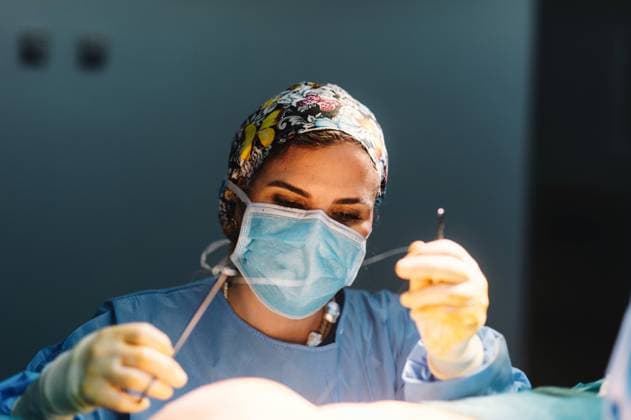 Plastic surgeon sewing up breast of female patient after inserting implants in operating room, Model released Copyright: xGabrielxTrujillox MR