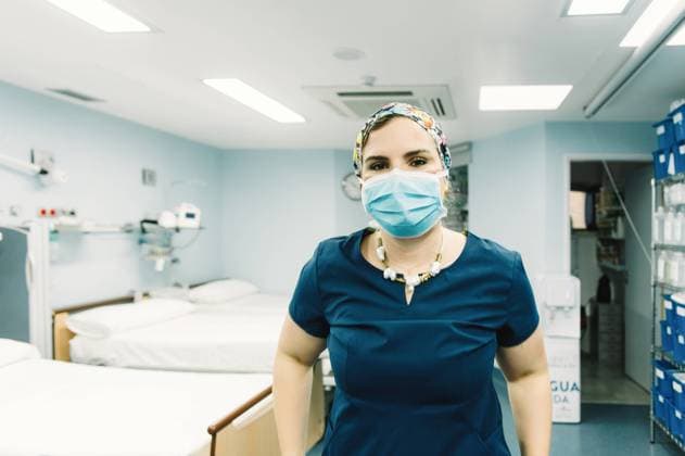 Female medic in blue uniform and protective mask standing in ward with empty beds and looking at camera, Model released Copyright: xGabrielxTrujillox MR