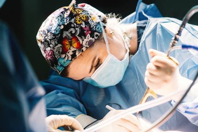 Side view of serious young doctor in protective mask and cap making surgery with instruments and crop nurse, Model released Copyright: xGabrielxTrujillox MR