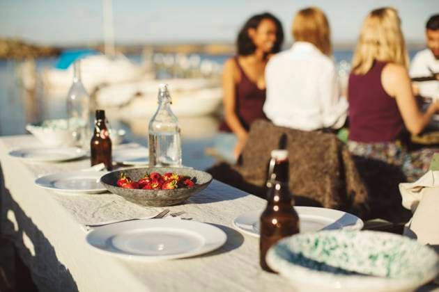 Fruits with plates and bottles on table against friends at harbor during sunny day , model released Copyright: xMaskotx , MA58590
