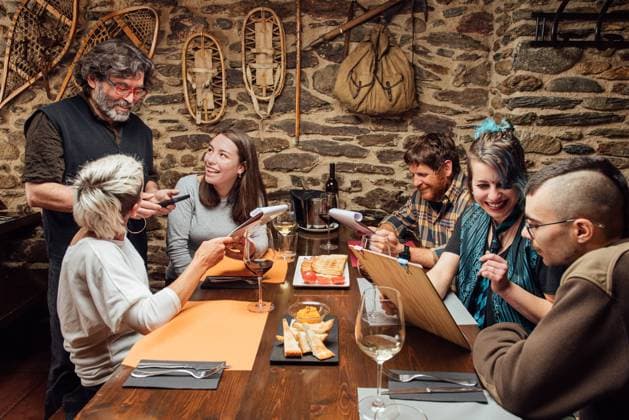 IMAGO Creative: Landleben - Essen Cheerful group of hipsters sitting at wooden table with menu and talking to waiter while ordering food during date in cafe, Model released, Property released Copyright: xGaldricxPenarrojax MR
