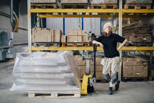 Full length of confident worker standing by stacked planks on pallet jack at industry , model released, property released Copyright: xMaskotx , MA60618