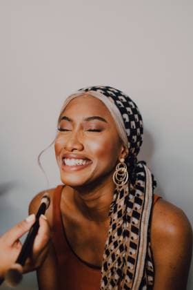 Attractive Black adult female applying eye shadow from professional makeup artist in studio Copyright: xGenessaxPanaintex Model Released