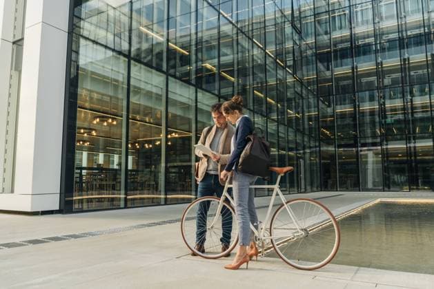 IMAGO Creative: Corporate: Klimaschutz, Digitalisierung und Urbanisierung Cheerful man and woman with bicycle smiling and looking at a tablet while communicating outside office building on modern city street, Model released Copyright: xHernandezxAndxSorokinax MR