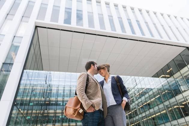 From below happy couple coworkers kissing each other while standing outside modern building on city street after work, Model released Copyright: xHernandezxAndxSorokinax MR