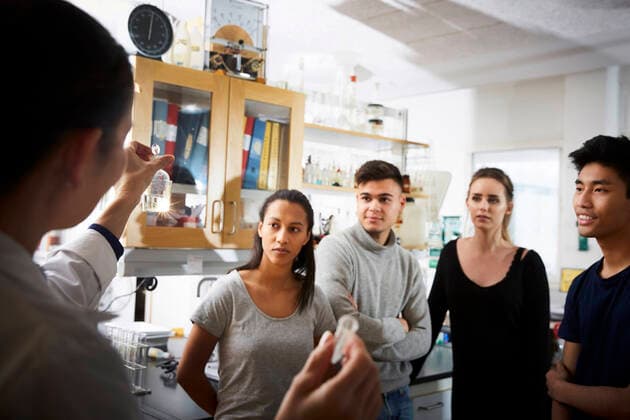 IMAGO Creative: Bildung, Wissenschaftserziehung Rear view of mature female teacher showing solution while explaining to young multi-ethnic students in laboratory , model released, property released Copyright: xMaskotx , MA62632
