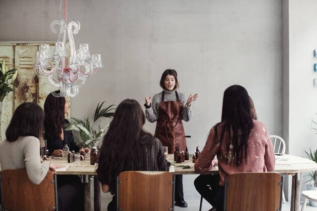 Confident female entrepreneur explaining to colleagues sitting at table in perfume workshop , model released, property released Copyright: xMaskotx , MA62783