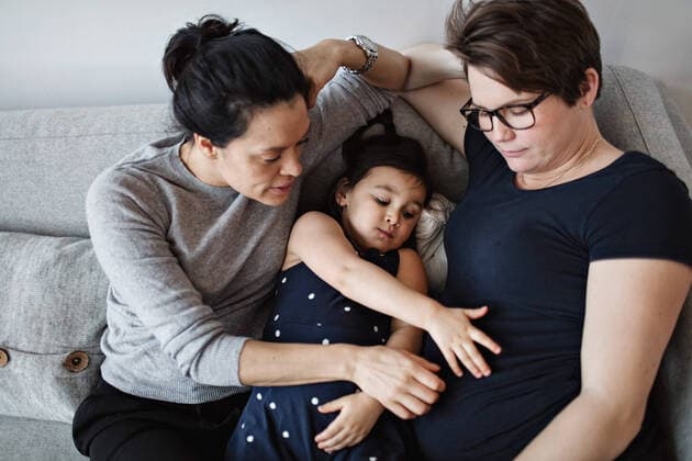 IMAGO Creative: Pride Month 2022, Engagement der Jugendlichen IMAGO Creative: Pride Month, Juni 2022, Pärchen und Familien High angle view of mother and daughter touching woman s abdomen while leaning on sofa at home , model released, property released Copyright: xMaskotx , MA63054