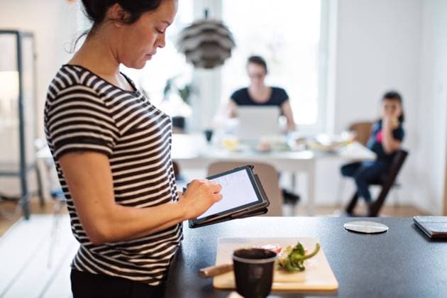 IMAGO Creative, Gesellschaft, Immer mehr Menschen haben Angst vor der Zukunft Woman making food while using digital tablet at kitchen with family in background , model released, property released Copyright: xMaskotx , MA63116