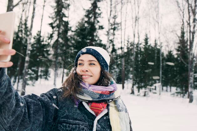 IMAGO Creative: Wintersport, Mode Smiling woman taking selfie through mobile phone while standing against trees on snowy field , model released Copyright: xMaskotx , MA64158