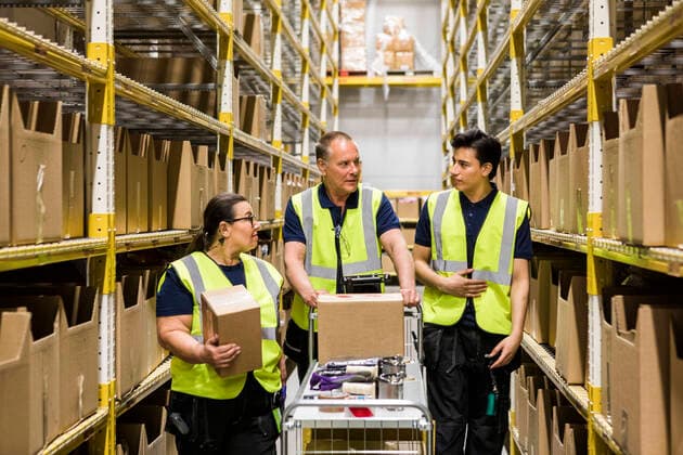 Multi-ethnic coworkers discussing while walking with cart on aisle amidst racks at distribution warehouse , model released, property released Copyright: xMaskotx , MA65203