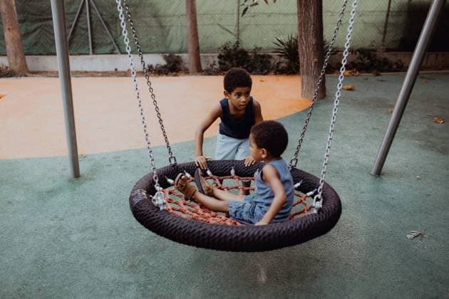 IMAGO Kreativ: Bruderschaft African American boy looking away and pushing swing with little brother while playing on playground together Copyright: xIsabelxAlcainex Model Released