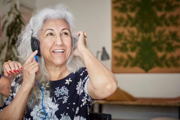 Smiling senior woman wearing headphones looking away while sitting with friend at home , model released, property released Copyright: xMaskotx , MA65688
